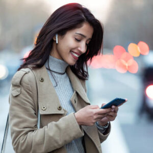 Shot of pretty young woman listening to music with wireless earphones and the smartphone in the street.